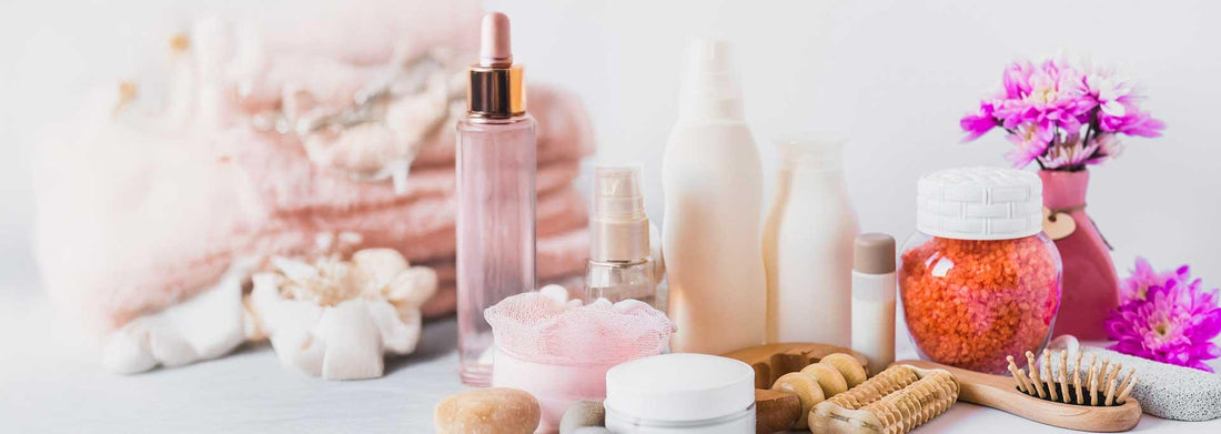 Skincare and bath essentials including pink serum, body scrub, brushes, and floral accents for self-care routine