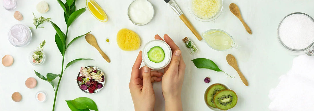 Hands holding cucumber slice on cream, surrounded by natural skincare ingredients and tools for DIY beauty routine