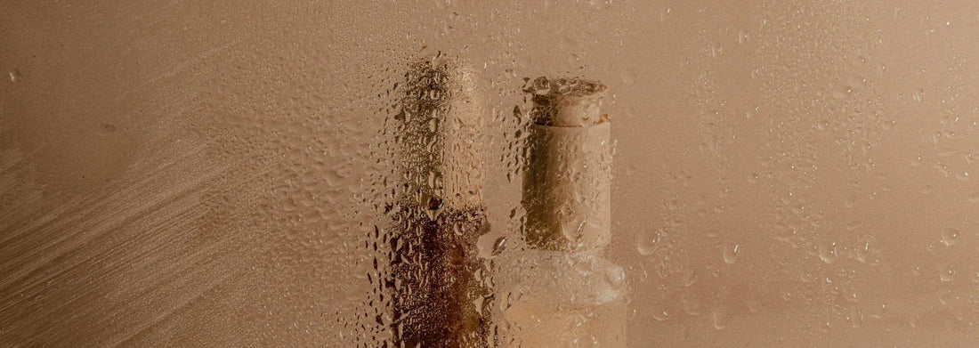 Moisturizing face serum bottle behind fogged glass with water droplets, soft beige background